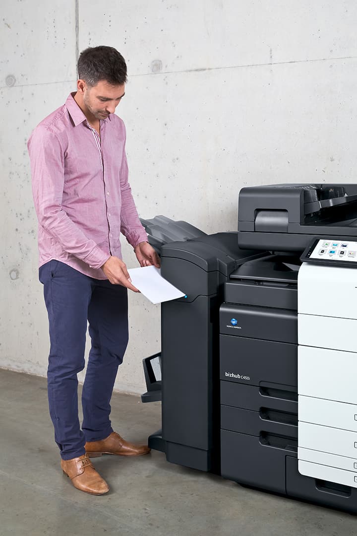 Image of a man in a smart pink blouse, and smart blue trousers, putting some paper into the printer